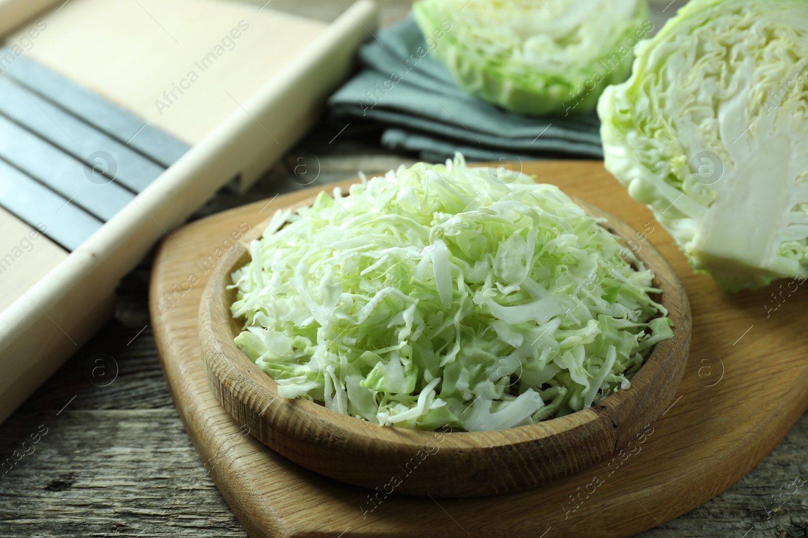 Photo of Fresh shredded cabbage and shredder on wooden table, closeup