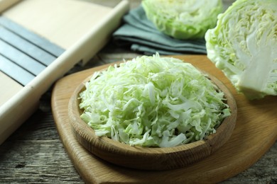 Photo of Fresh shredded cabbage and shredder on wooden table, closeup