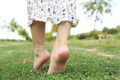 Photo of Woman walking barefoot on green grass outdoors, closeup