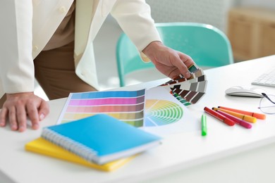 Photo of Designer with color samples working at table in office, closeup