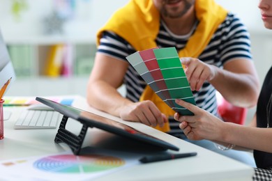 Photo of Designers with color samples working together at table in office, closeup