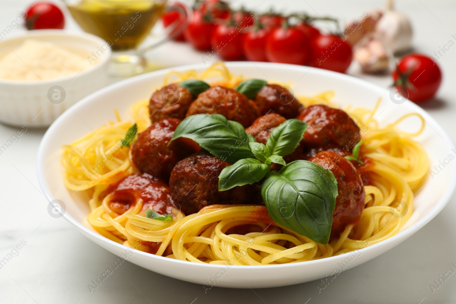 Photo of Delicious pasta with meatballs and ingredients on white marble table, closeup