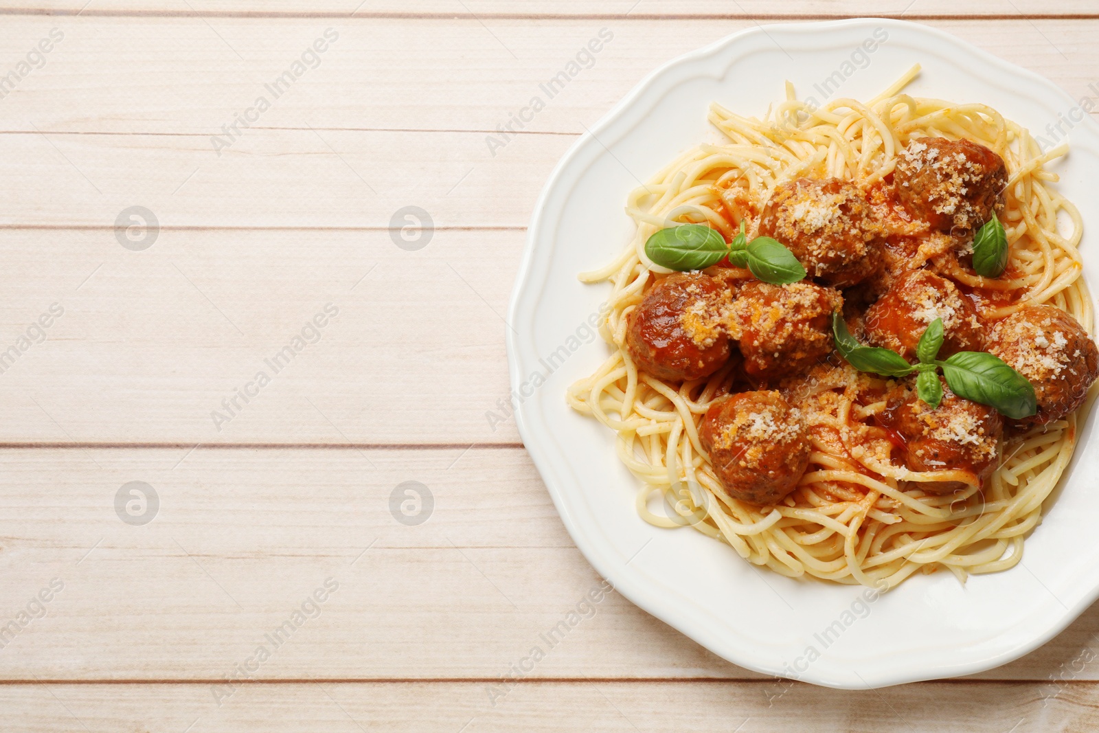 Photo of Delicious pasta with meatballs on light wooden table, top view. Space for text