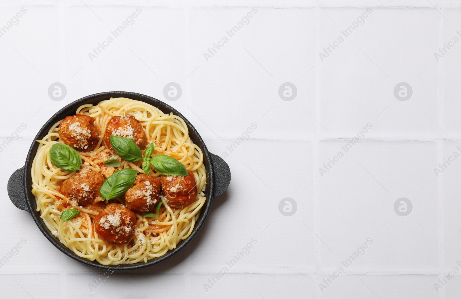 Photo of Delicious pasta with meatballs on white tiled table, top view. Space for text