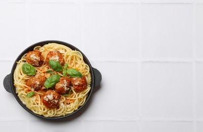 Photo of Delicious pasta with meatballs on white tiled table, top view. Space for text