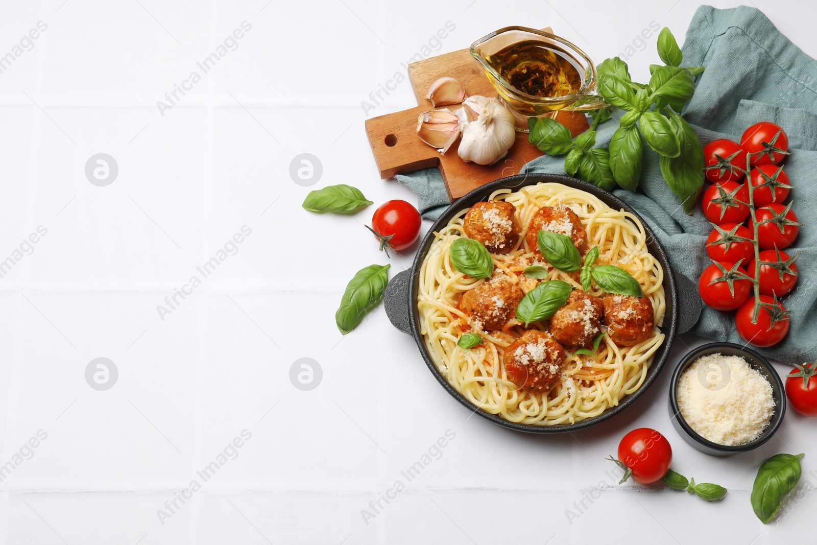 Photo of Delicious pasta with meatballs and ingredients on white tiled table, flat lay. Space for text