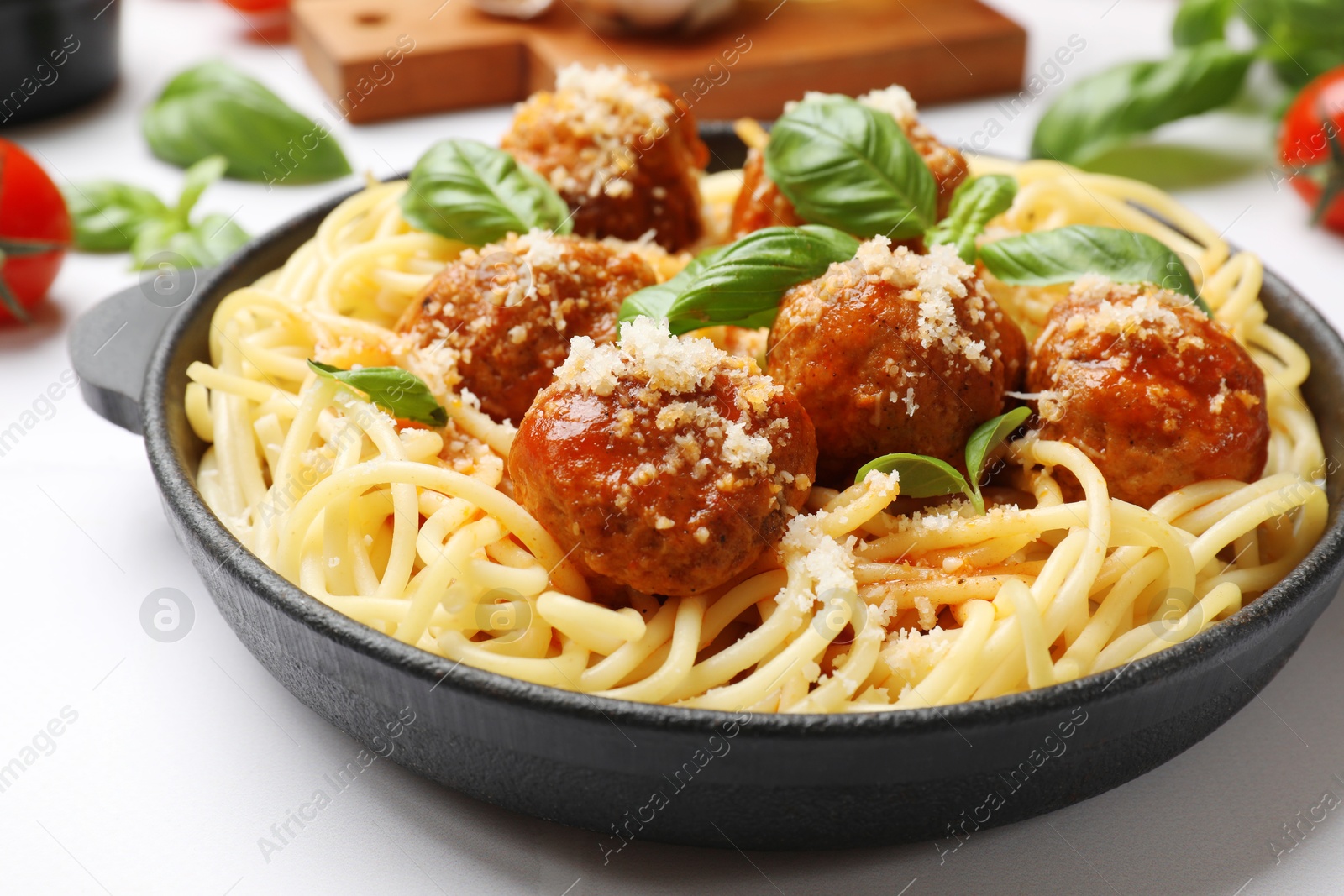 Photo of Delicious pasta with meatballs and ingredients on white tiled table, closeup