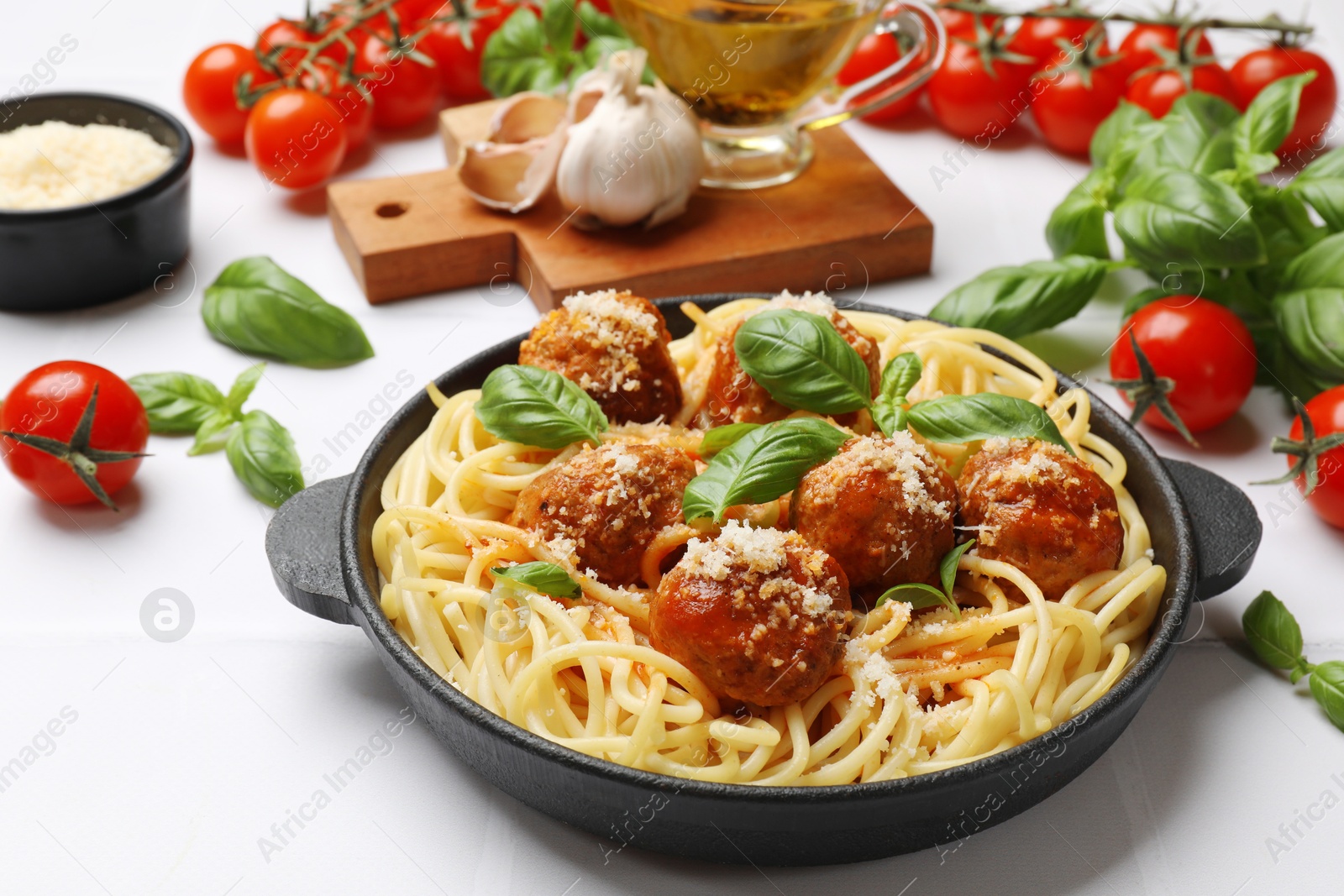 Photo of Delicious pasta with meatballs and ingredients on white tiled table, closeup