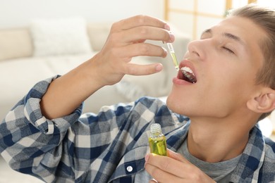 Photo of Young man taking CBD tincture indoors. Herbal extract