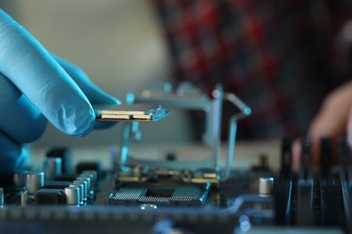 Photo of Man installing computer chip onto motherboard at table, closeup