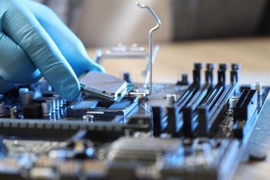 Photo of Man installing computer chip onto motherboard at table, closeup