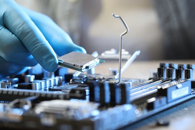 Man installing computer chip onto motherboard at wooden table, closeup