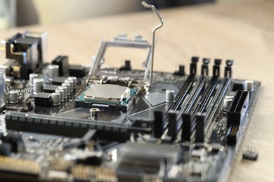 Photo of Motherboard with modern computer chip and other components on wooden table, closeup