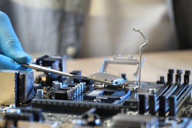 Photo of Man installing computer chip onto motherboard at table, closeup