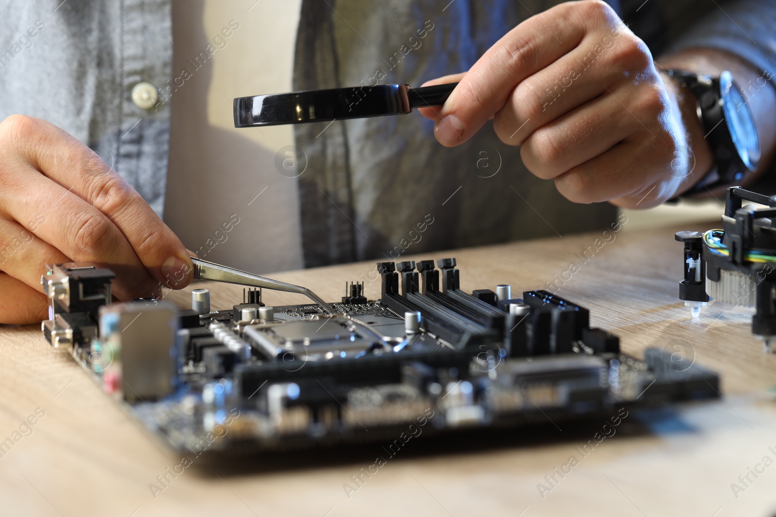 Photo of Man installing computer chip onto motherboard at wooden table, closeup