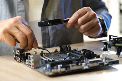 Photo of Man installing computer chip onto motherboard at wooden table, closeup