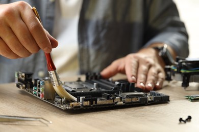 Man installing computer chip onto motherboard at wooden table, closeup