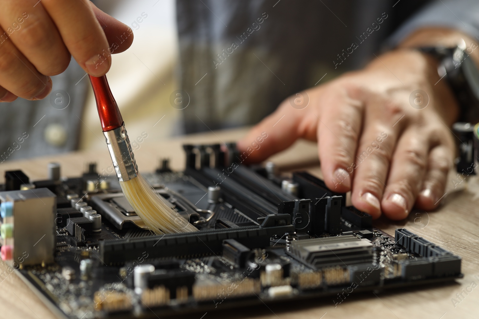 Photo of Man installing computer chip onto motherboard at wooden table, closeup