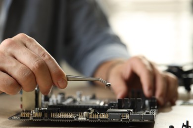 Photo of Man installing computer chip onto motherboard at wooden table, closeup