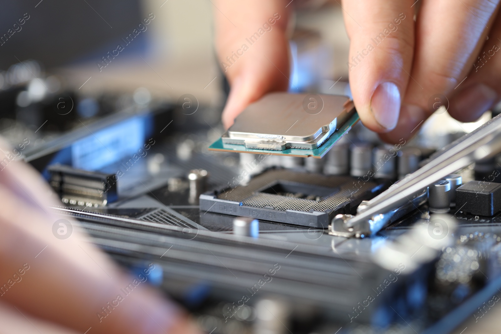 Photo of Man installing computer chip onto motherboard at table, closeup