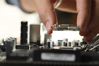 Man installing computer chip onto motherboard at table, closeup