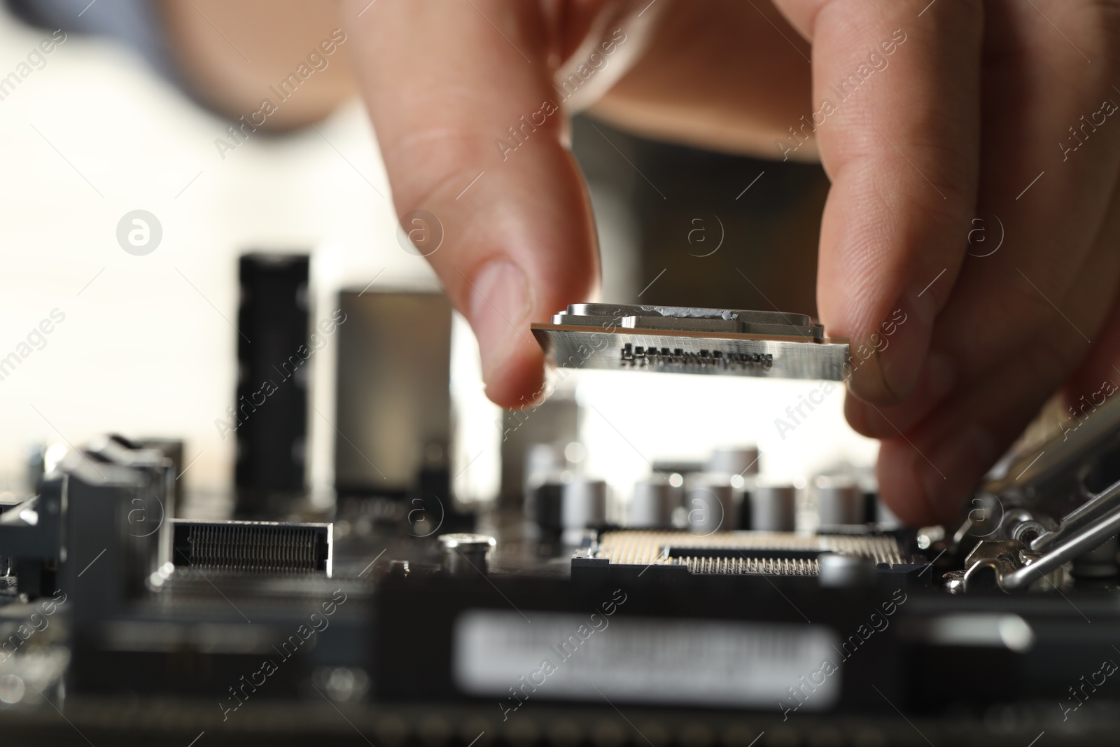 Photo of Man installing computer chip onto motherboard at table, closeup