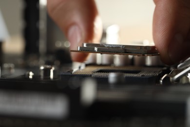 Man installing computer chip onto motherboard at table, closeup