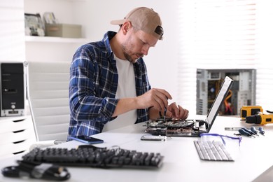 Photo of Man installing motherboard into laptop at white table