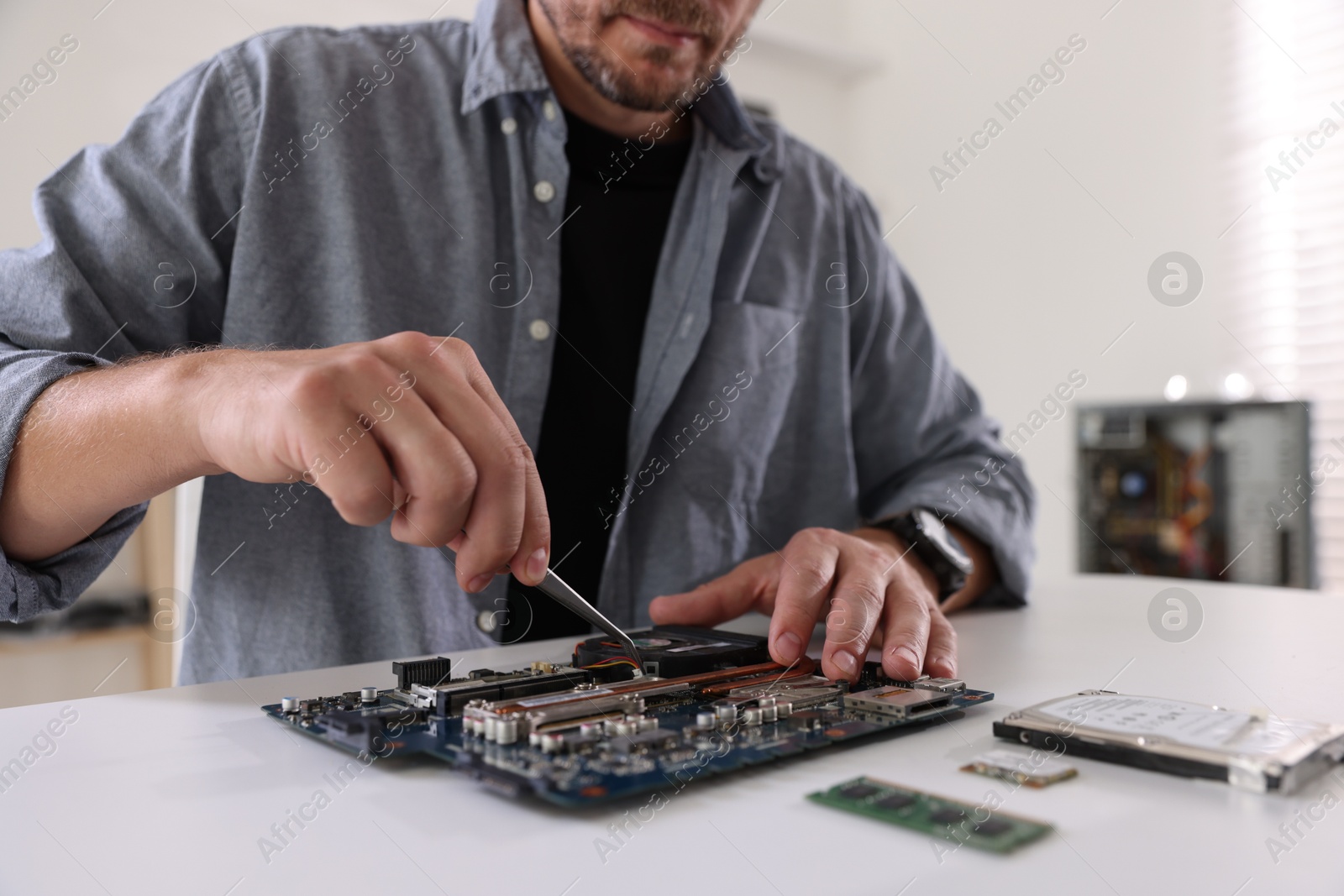 Photo of Man installing computer chip onto motherboard at white table, closeup