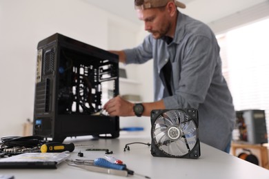 Man installing fan into computer at white table, selective focus