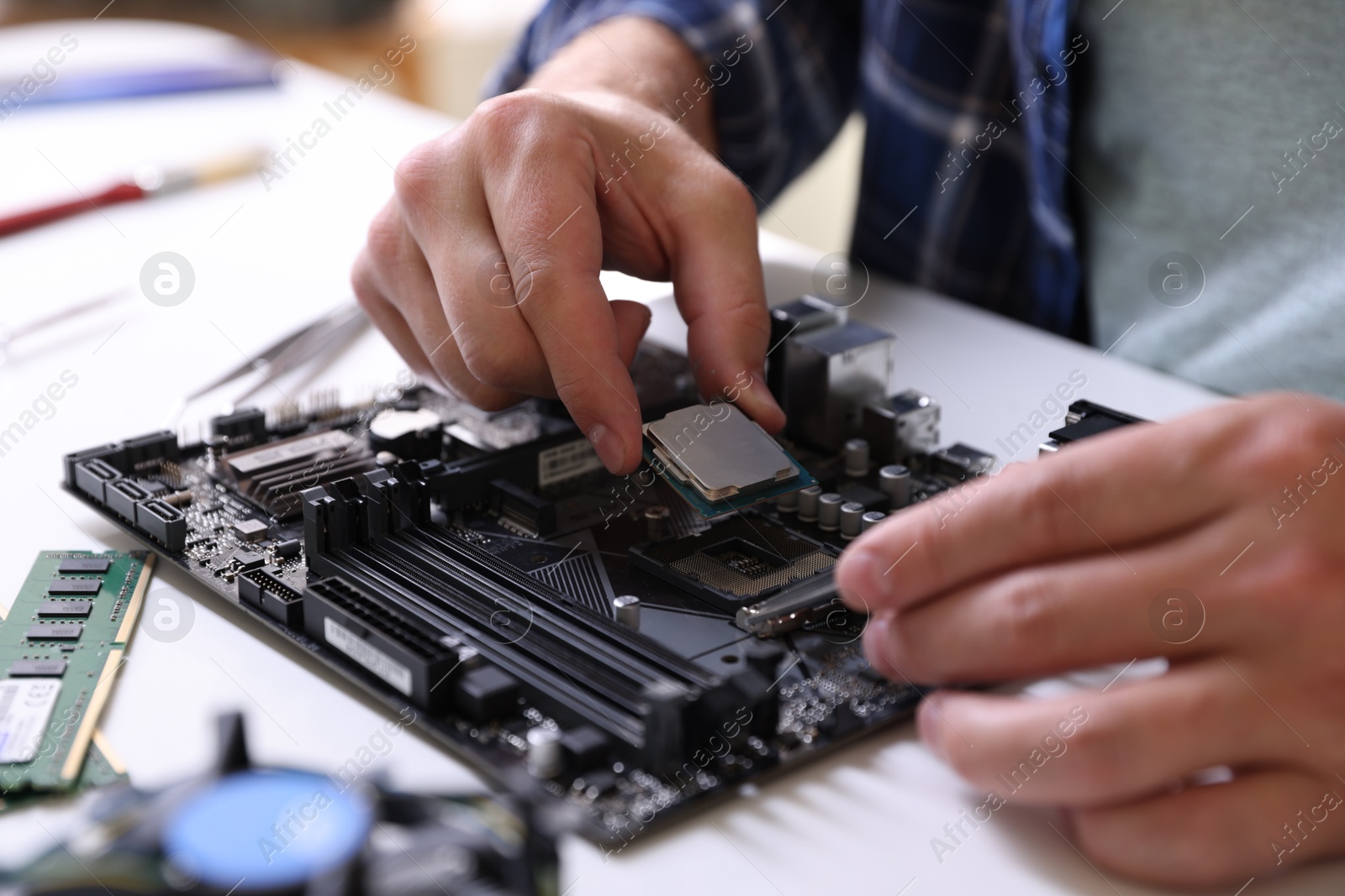 Photo of Man installing computer chip onto motherboard at white table, closeup