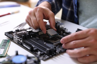 Photo of Man installing computer chip onto motherboard at white table, closeup