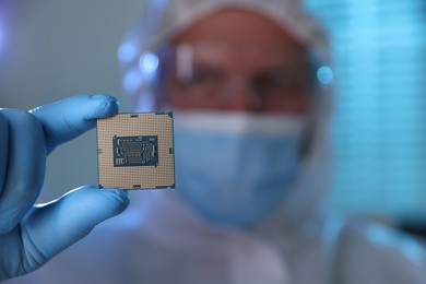 Man in mask holding computer chip on blurred background, selective focus