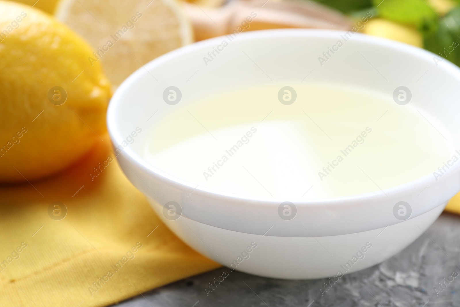 Photo of Fresh lemon juice in bowl and fruit on grey table, closeup