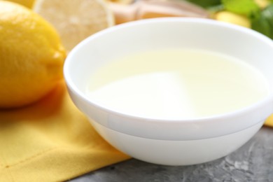 Photo of Fresh lemon juice in bowl and fruit on grey table, closeup