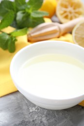 Photo of Fresh lemon juice in bowl, fruits, mint and squeezer on grey table, closeup