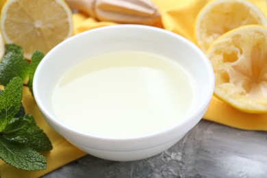 Photo of Fresh lemon juice in bowl, mint and fruits on grey table, closeup