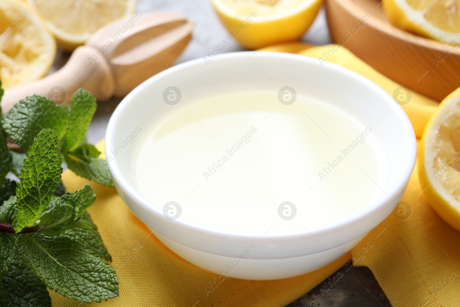 Photo of Fresh lemon juice in bowl, fruits, mint and squeezer on table, closeup