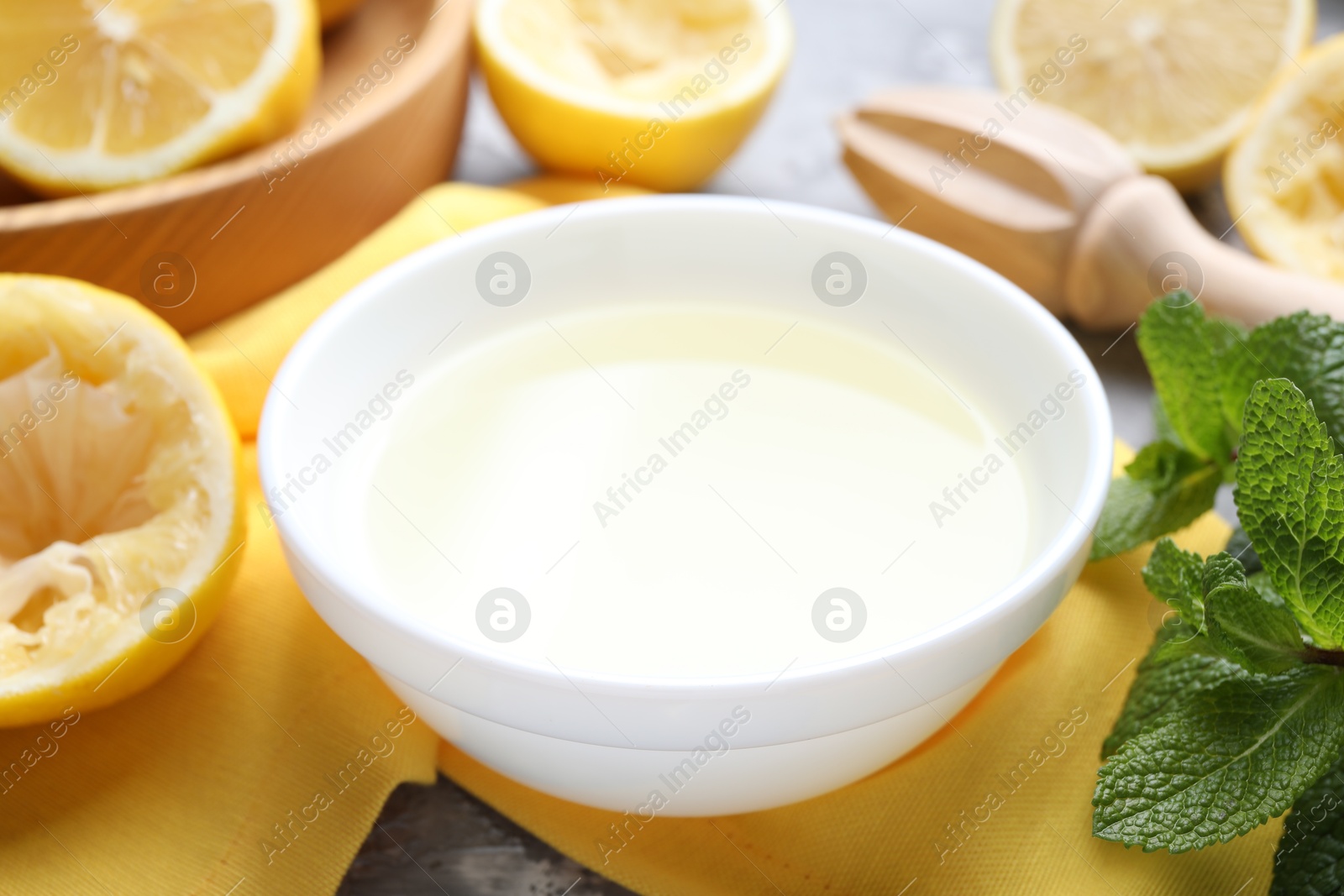 Photo of Fresh lemon juice in bowl, fruits, mint and squeezer on table, closeup