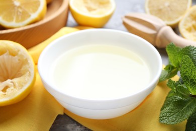 Fresh lemon juice in bowl, fruits, mint and squeezer on table, closeup