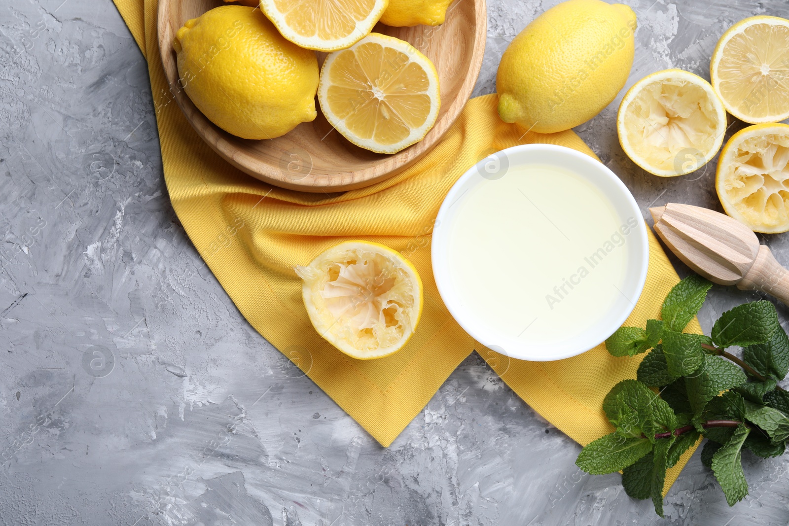 Photo of Fresh lemon juice in bowl, fruits, mint and squeezer on grey table, top view