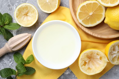 Photo of Fresh lemon juice in bowl, fruits, mint and squeezer on grey table, top view