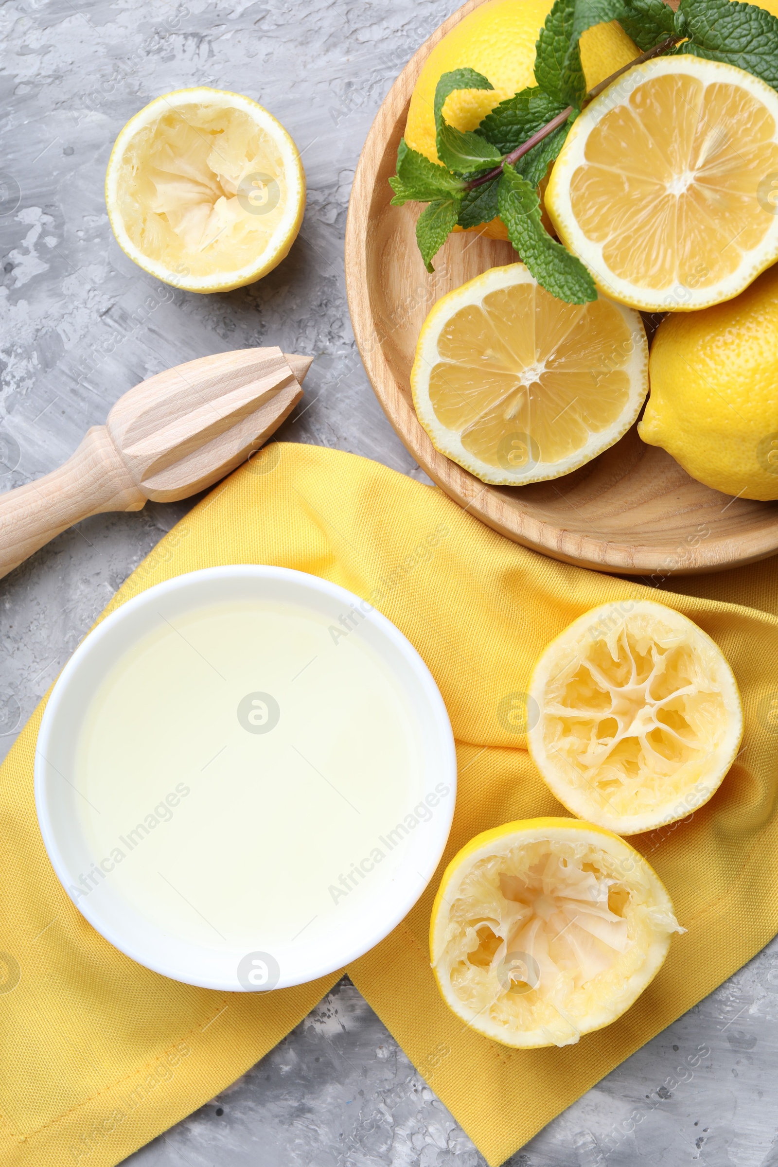 Photo of Fresh lemon juice in bowl, fruits, mint and squeezer on grey table, top view