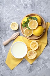 Fresh lemon juice in bowl, fruits, mint and squeezer on grey table, top view