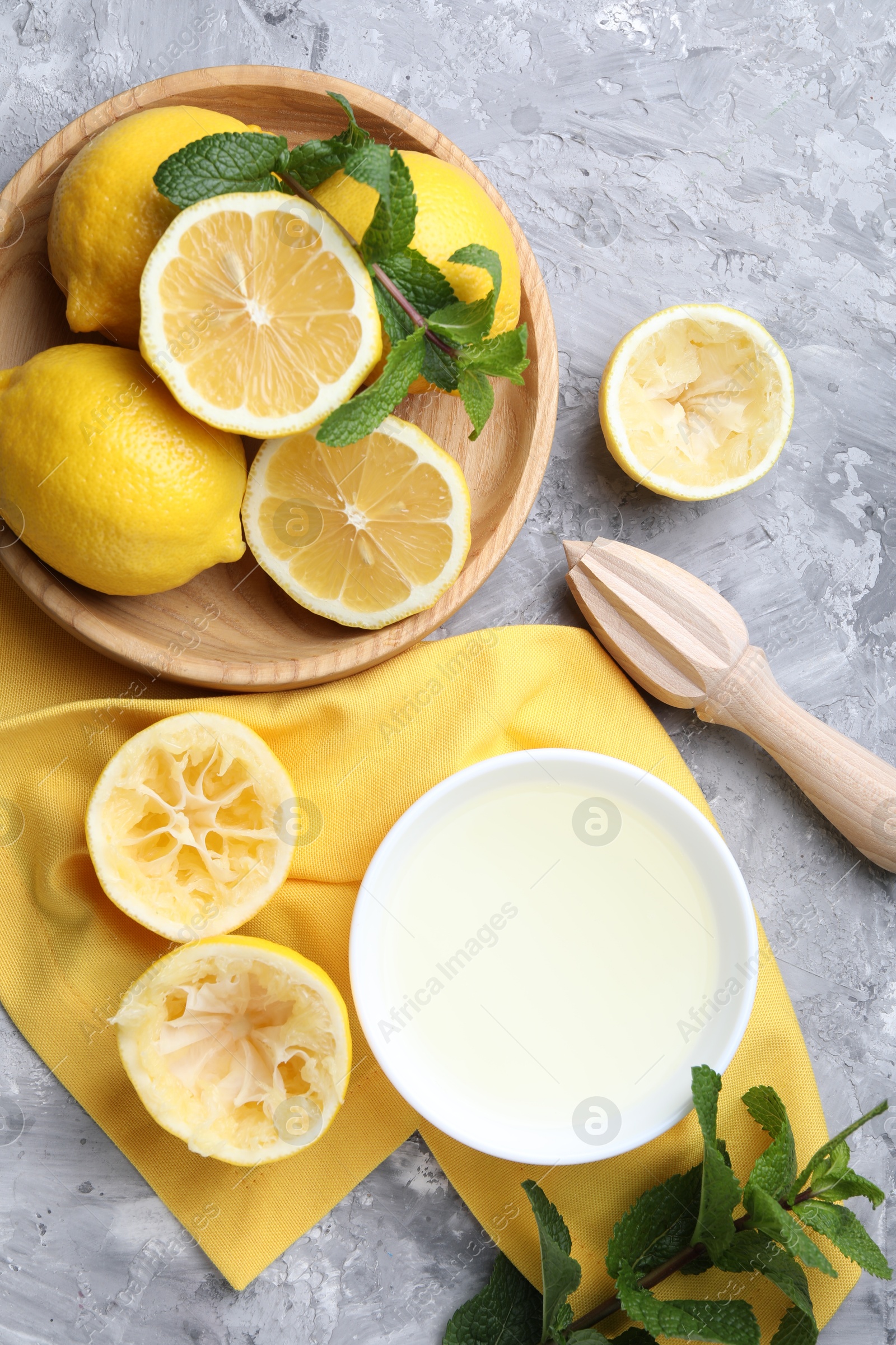 Photo of Fresh lemon juice in bowl, fruits, mint and squeezer on grey table, top view