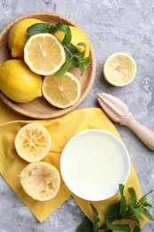 Fresh lemon juice in bowl, fruits, mint and squeezer on grey table, top view