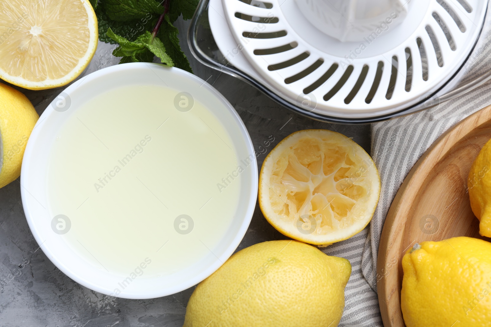 Photo of Fresh lemon juice in bowl, fruits, mint and juicer on grey table, top view