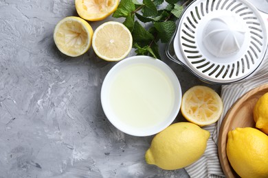 Photo of Fresh lemon juice in bowl, fruits, mint and juicer on grey table, top view. Space for text