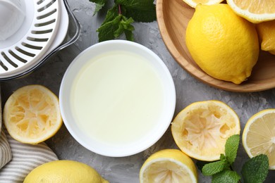 Photo of Fresh lemon juice in bowl, fruits, mint and juicer on grey table, top view