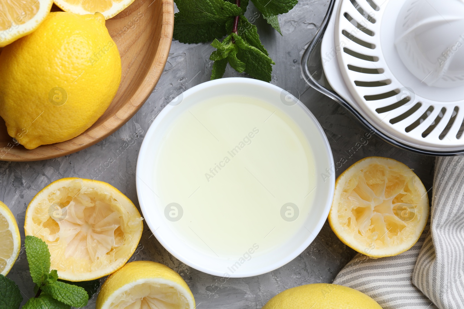 Photo of Fresh lemon juice in bowl, fruits, mint and juicer on grey table, top view